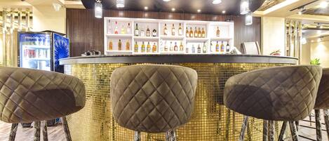 A bar area with a round counter, cushioned bar stools, and a variety of liquor bottles on shelves.