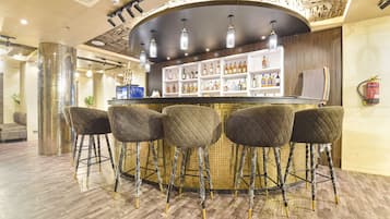 A bar area with a round counter, four cushioned stools, and a shelf with various bottles.