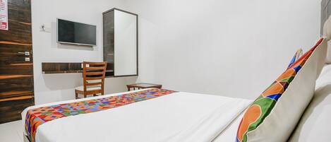 Ein Hotelzimmer mit Bett, Schreibtisch, Stuhl, Fernseher und Spiegel.