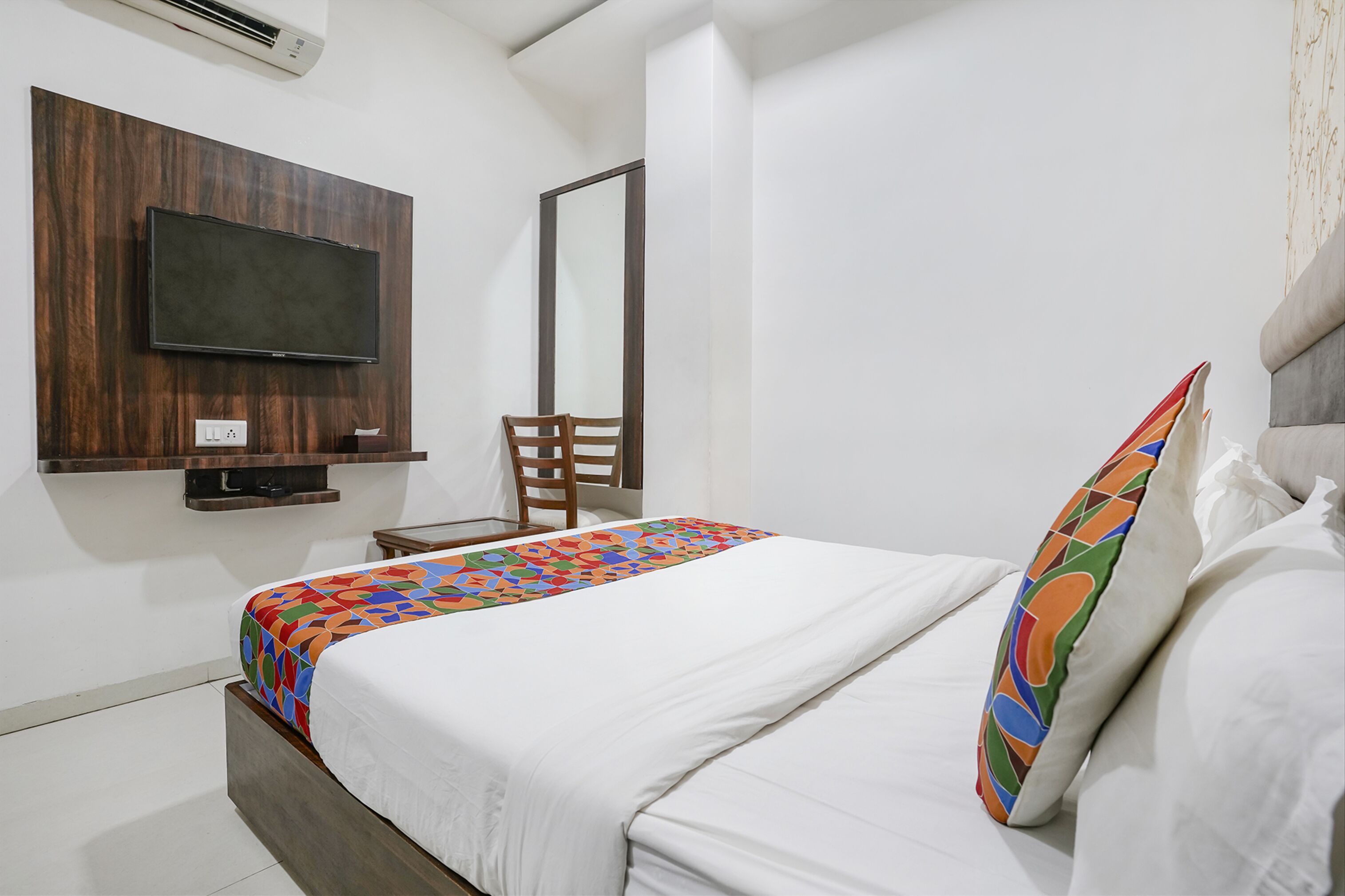 A hotel room with a bed, a TV mounted on the wall, a chair, and a mirror.