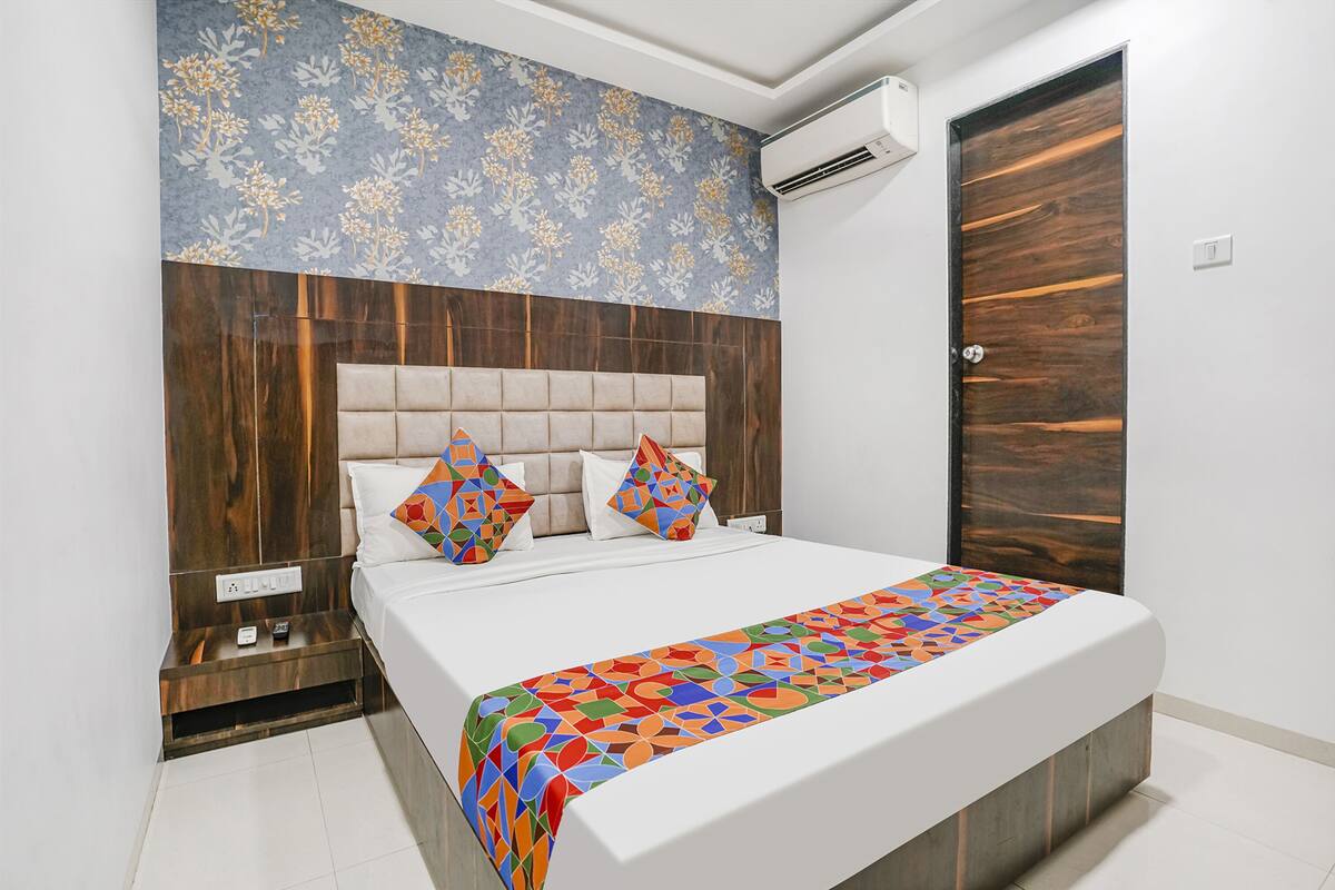 A neatly made bed with a colorful geometric-patterned bedspread, a tufted headboard, and a floral-patterned wall above.