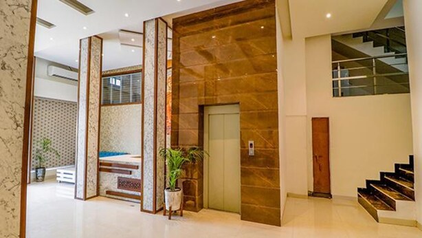 A modern lobby with a marble floor, a wooden reception desk, a potted plant, and a staircase. - Fabhotel Prime Parisar (Amritsar)