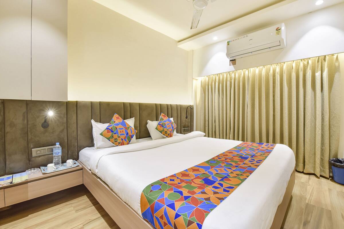 A hotel room with a bed, nightstand, and an air conditioning unit.