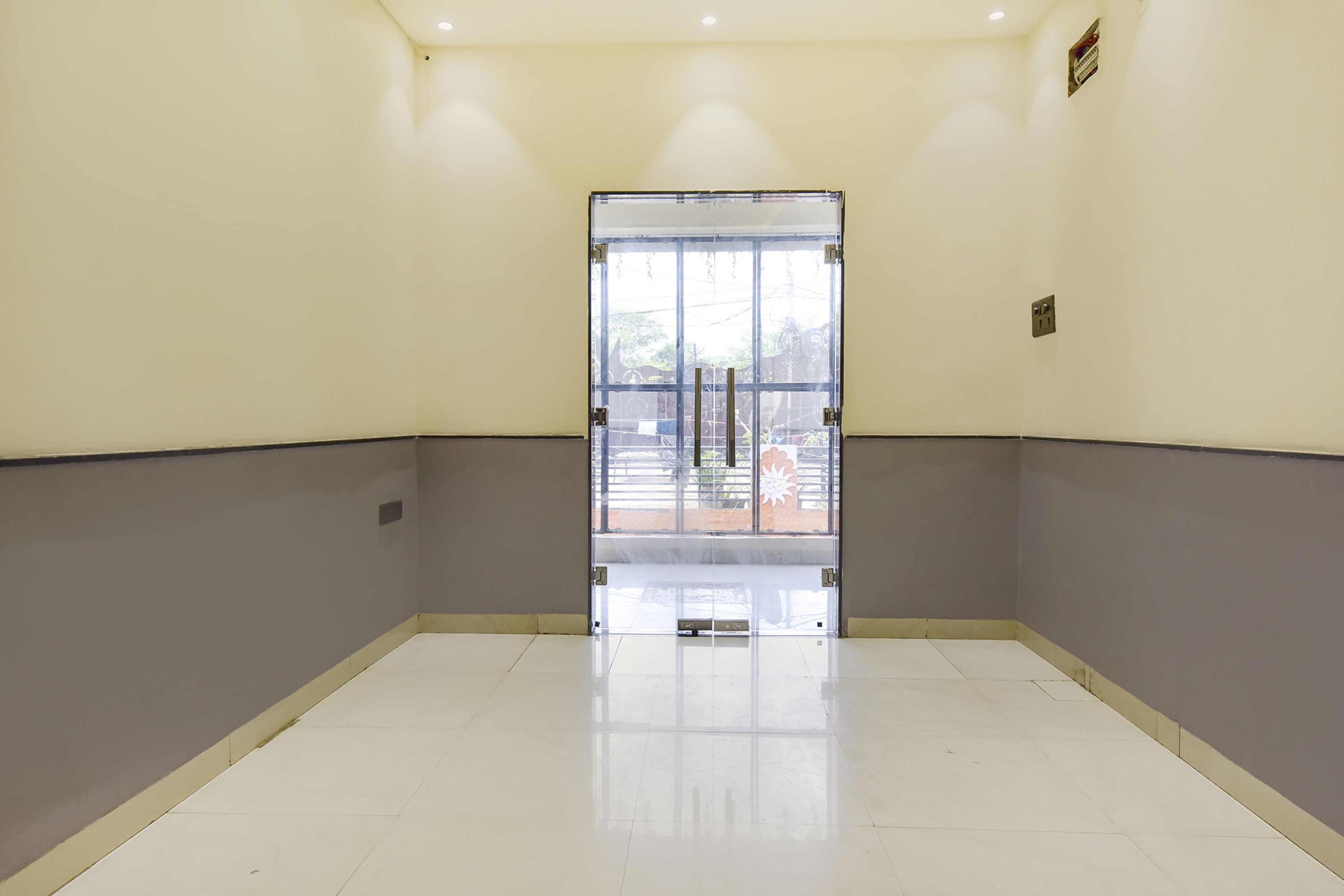 Un couloir avec une porte vitrée donnant sur un espace extérieur. Les murs sont peints dans une couleur claire et le sol est carrelé.