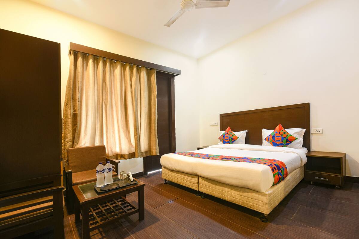 A hotel room with a bed, a nightstand, a chair, a table, and curtains.