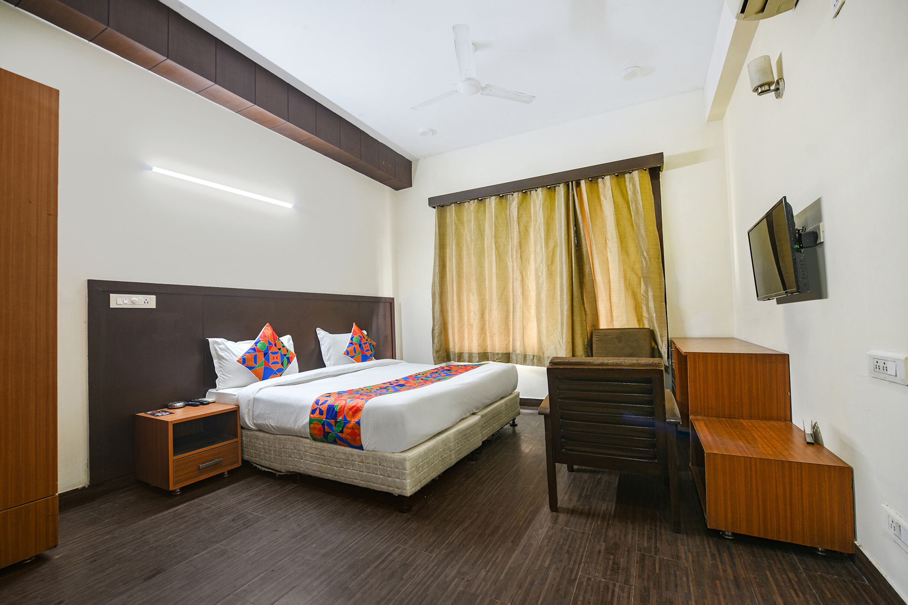 A hotel room with a bed, nightstand, desk, chair, and a TV mounted on the wall.