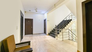 A spacious hallway with a wooden bench, a staircase with metal railings, and a ceiling fan. - Fabhotel Silver Tree (Gurugram)