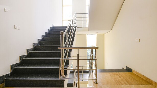 A staircase with a metal handrail, leading to a landing with a wooden floor. - Fabhotel Silver Tree (Gurugram)