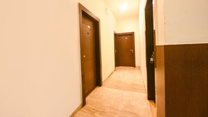 A narrow hallway with three closed doors, a tiled floor, and a ceiling light. - Fabhotel Silver Tree (Gurugram)