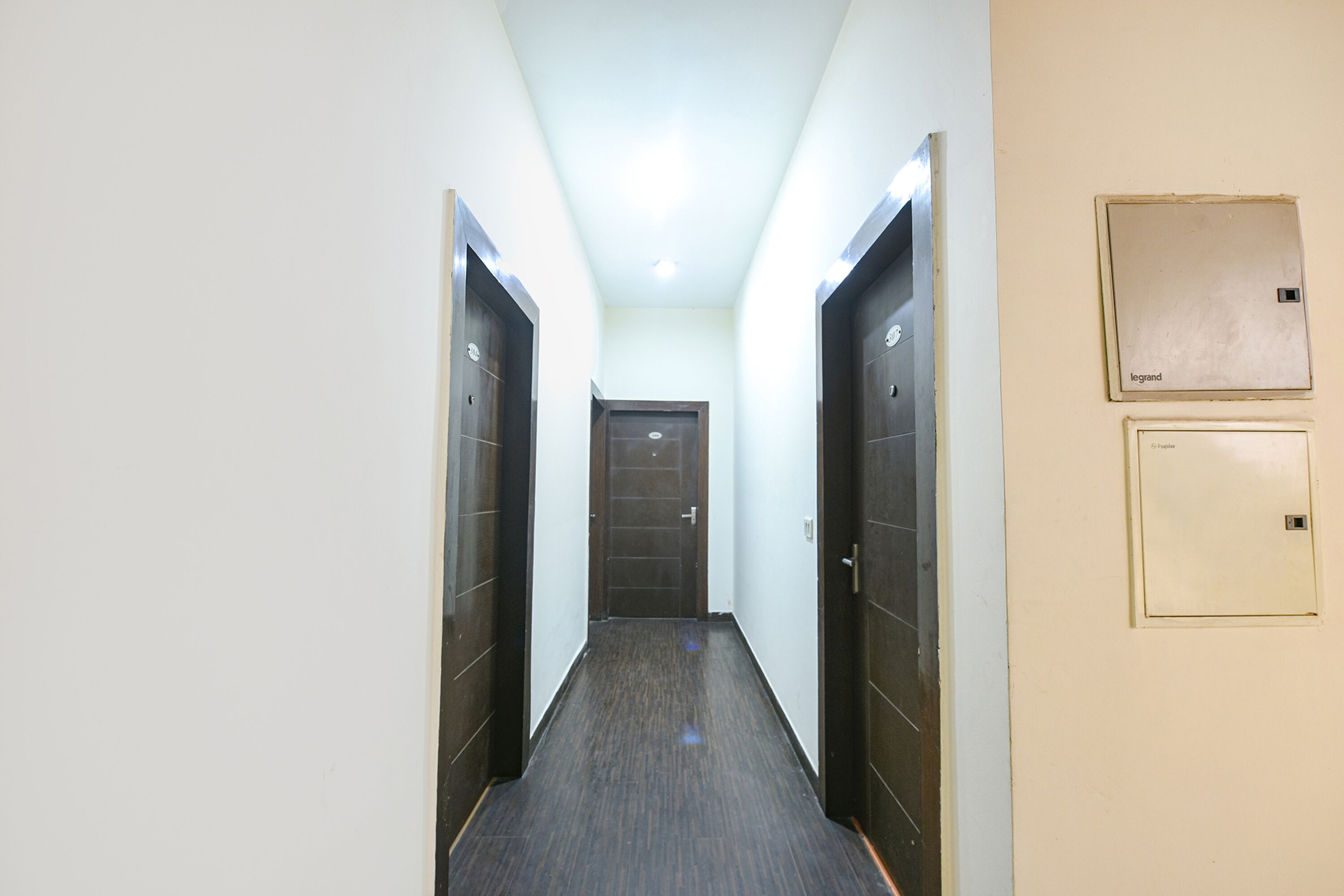 A narrow hallway with dark wooden doors on either side, a light-colored wall, and a ceiling light.