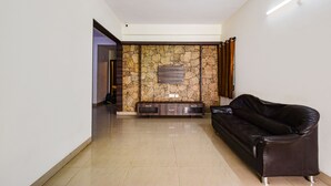 A spacious living area with a stone wall, a dark leather sofa, and a ceiling fan. - Fabhotel Rs (Hyderabad)