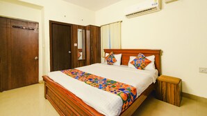 A bedroom with a wooden bed, a nightstand, an air conditioning unit, and a door. - Fabhotel Rs (Hyderabad)