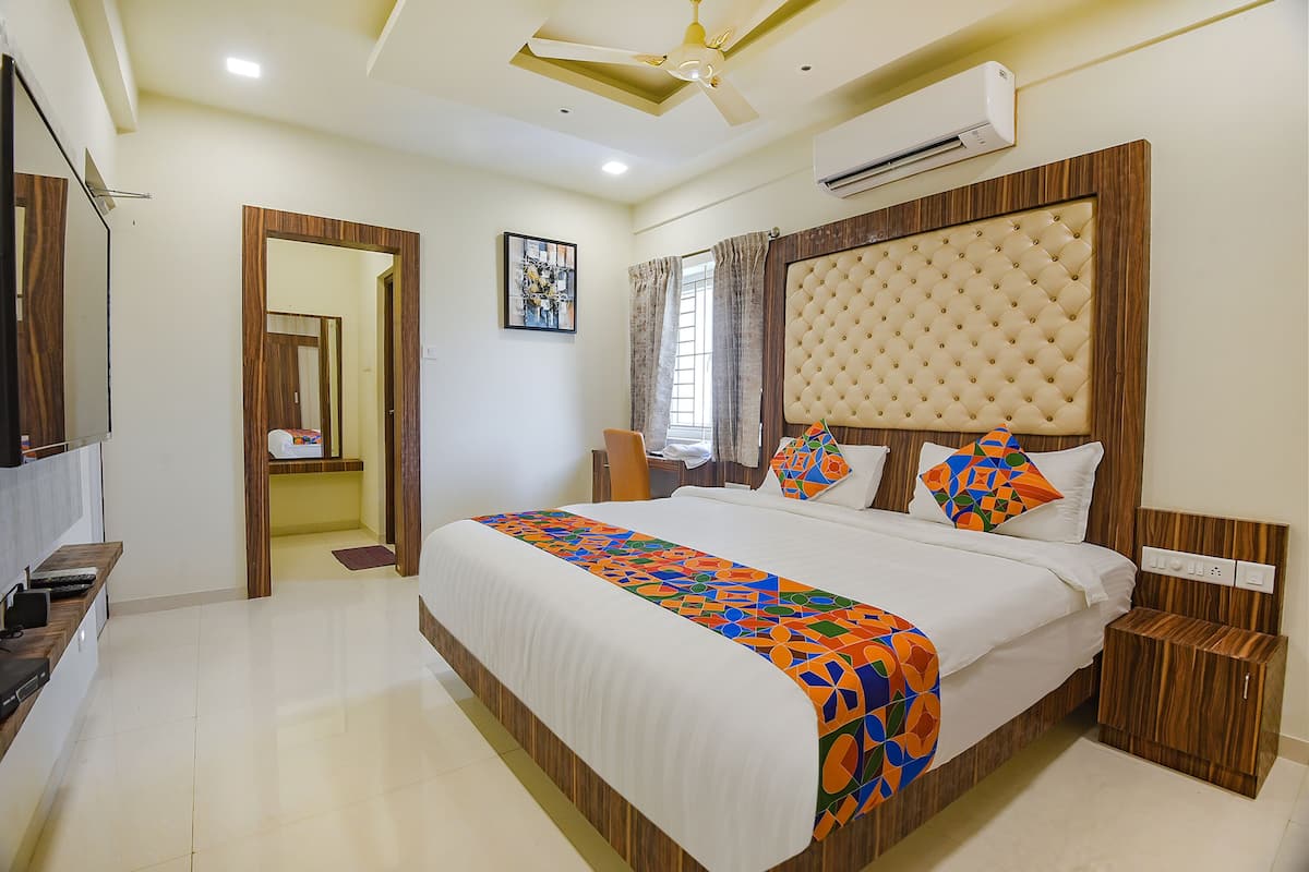 A hotel room with a large bed, a wooden headboard, an air conditioning unit, a bedside table, and a television.
