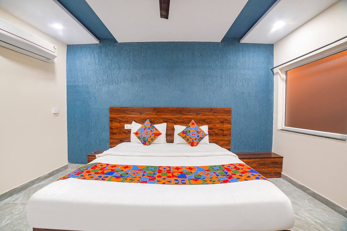 Un dormitorio con cama, cabecera, ventana y mesita de noche.
