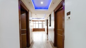 A hallway with wooden doors, a ceiling with blue lighting, and a number sign on the wall. - Fabhotel Lailas County (Puducherry)