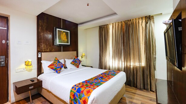 A hotel room with a bed, a nightstand, a TV, a painting on the wall, and a window with curtains. - Fabhotel Lailas County (Puducherry)