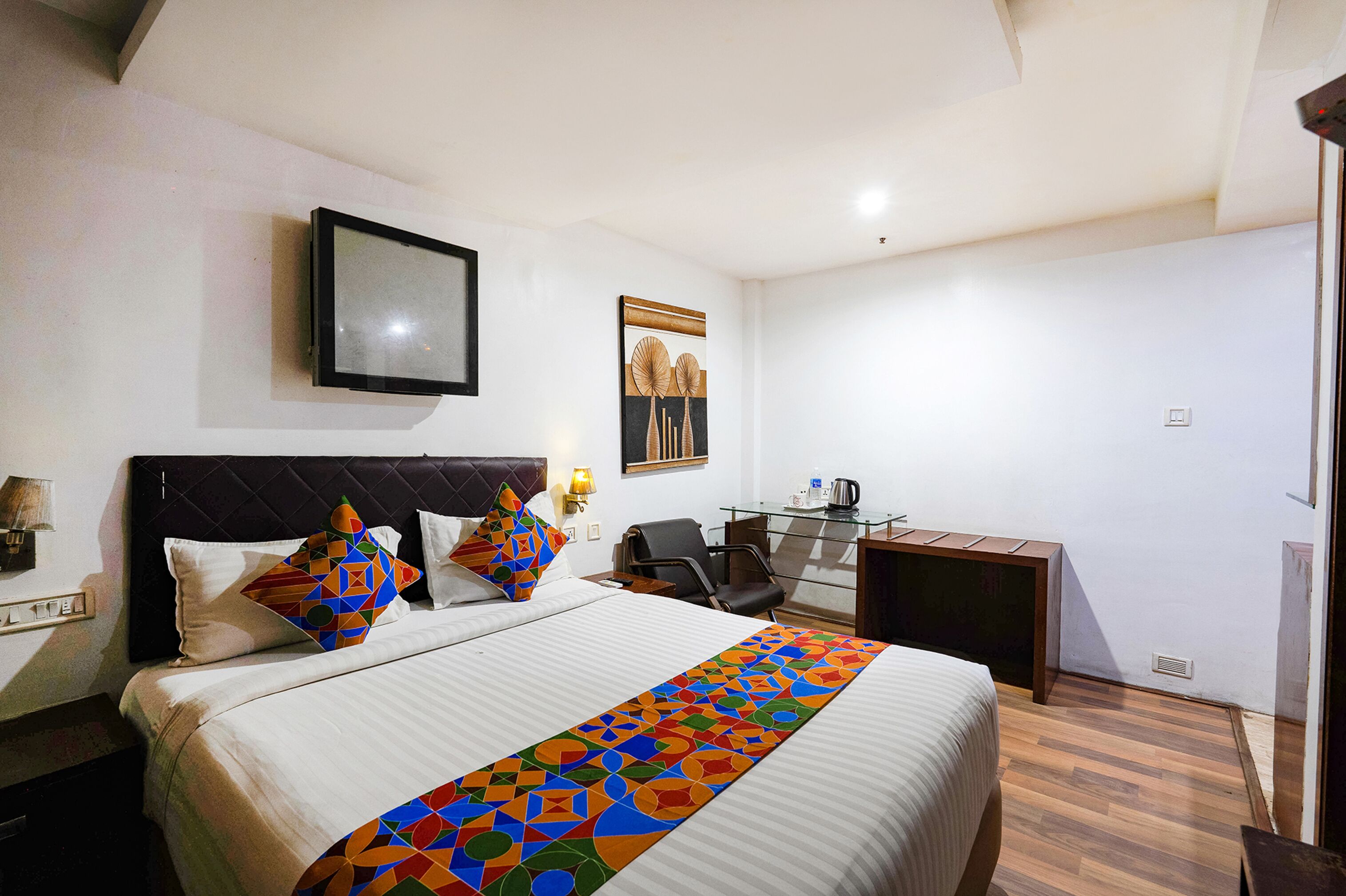 A hotel room with a bed, a desk, a chair, and a picture on the wall.