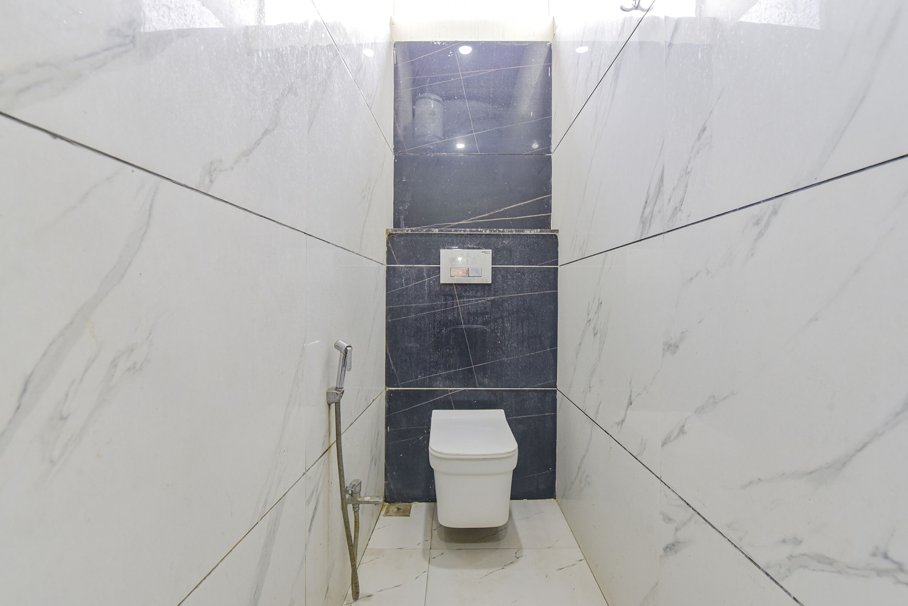 Ein kleines, schmales Badezimmer mit Toilette in Weiß und einer Wand aus dunklem Marmor.