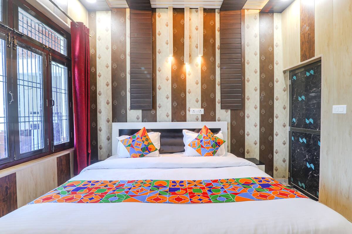 Una habitación de hotel con una cama grande, una ventana con rejas, una cortina roja y papel tapiz estampado.