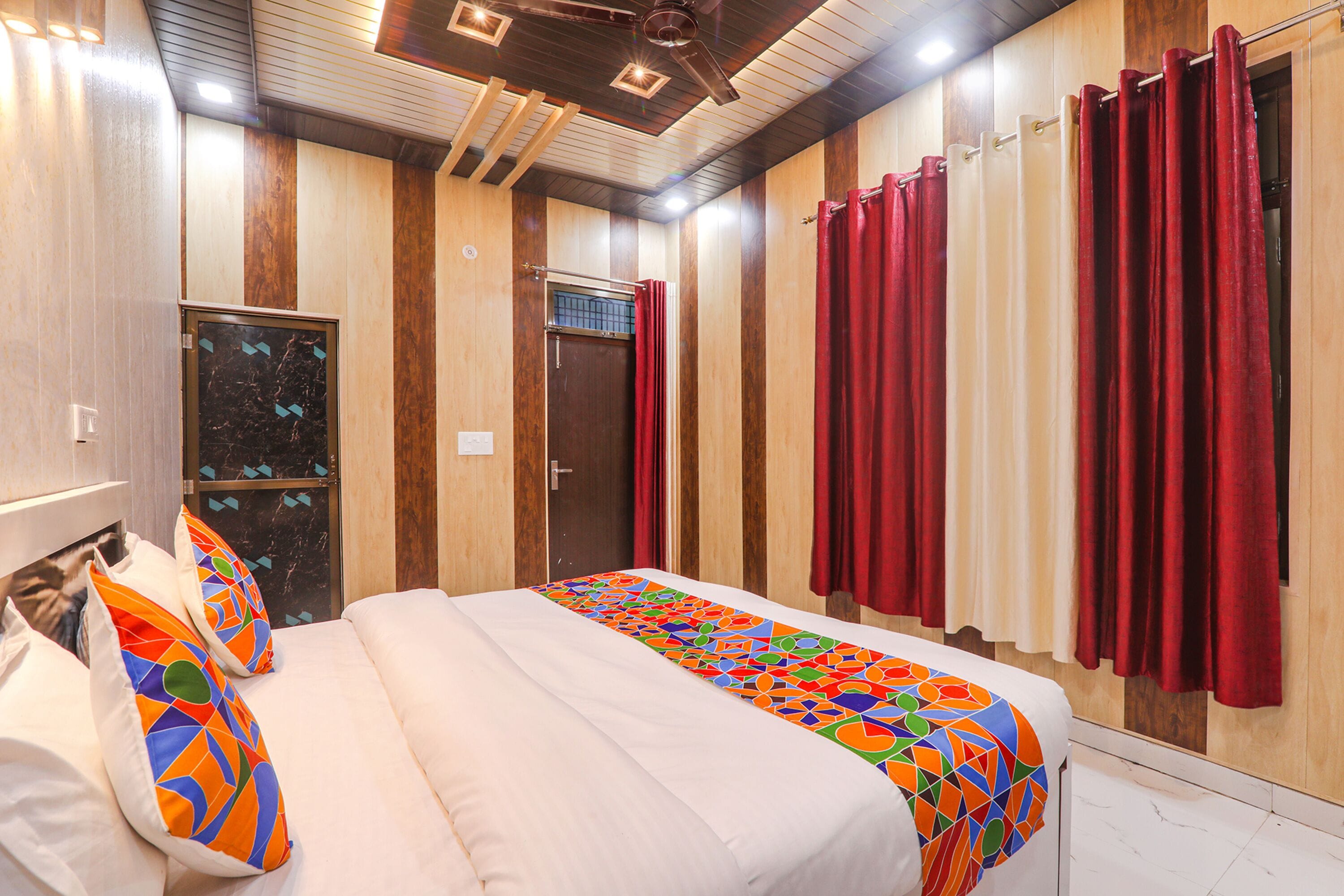 Una habitación de hotel con una cama, un ventanal con cortinas rojas y un panel de pared de madera.