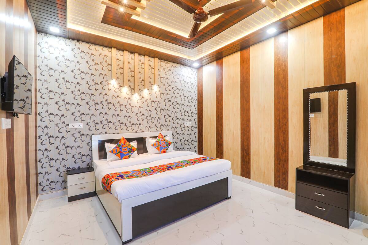Un dormitorio moderno con una cama grande, un armario de madera, un espejo y un televisor montado en la pared.
