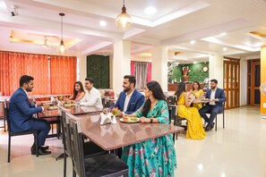 A dining area with multiple tables and chairs, a ceiling fan, and a decorative wall. - Fabhotel Shree Swami (Pune)