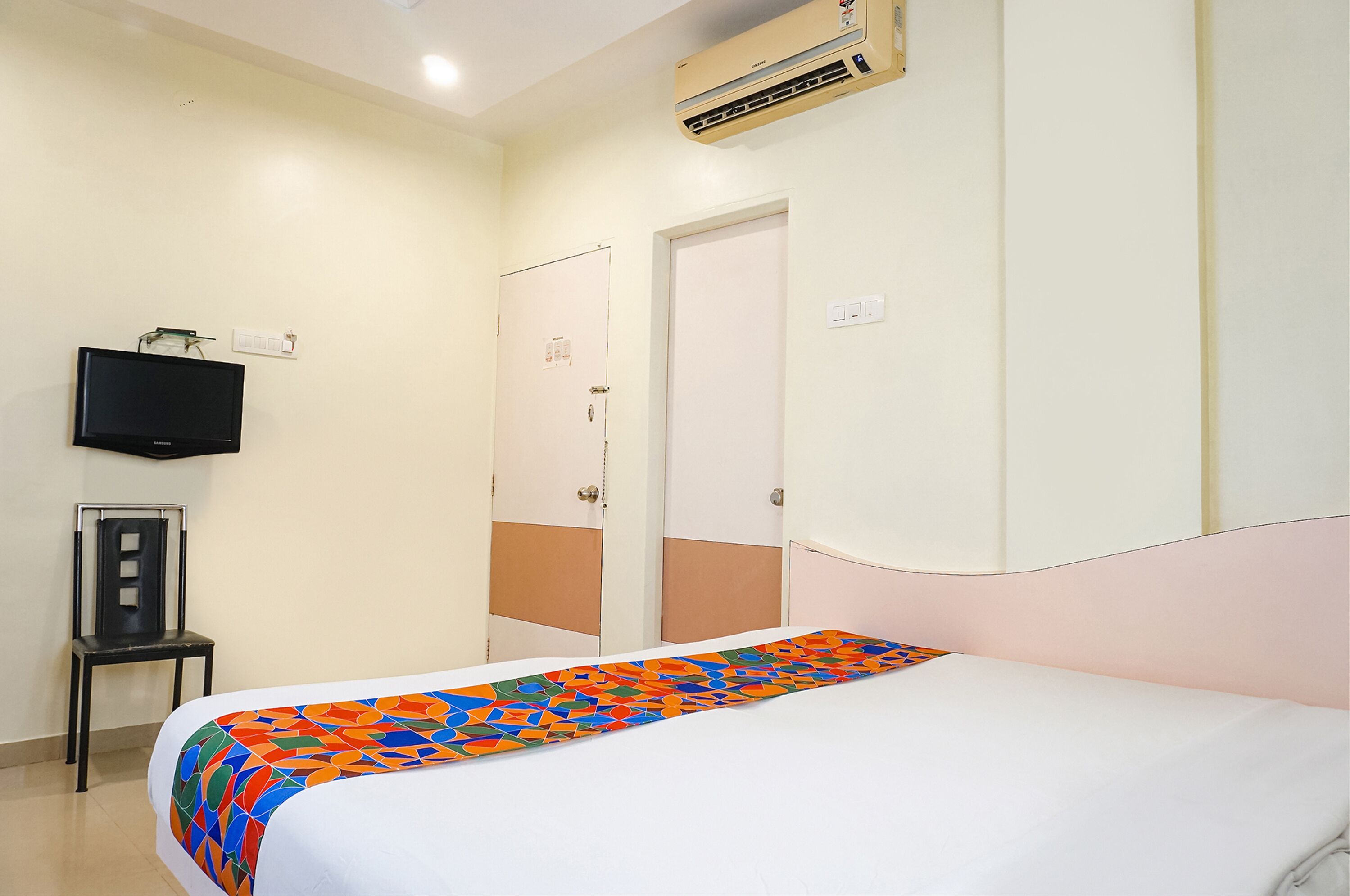 Una habitación de hotel con cama, televisión en la pared y puerta con interruptor de luz.