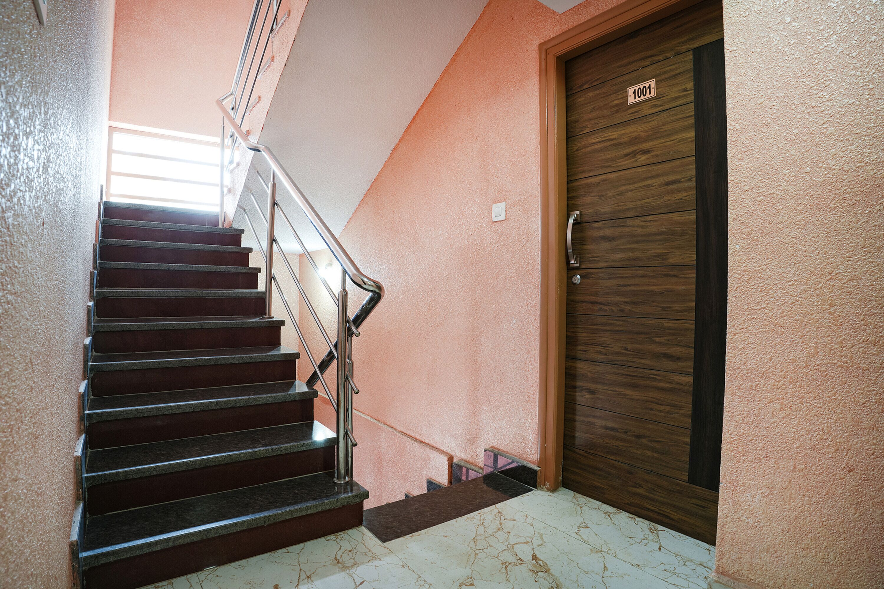 Una escalera con barandilla metálica que conduce a una puerta de madera con el número 1001.