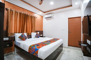 Une chambre d’hôtel avec un lit, des rideaux, un appareil de climatisation, une porte et un téléviseur.