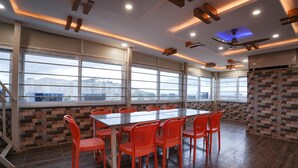 Uma sala de conferências com uma mesa grande e cadeiras laranja, grandes janelas com vista e um design de teto moderno.