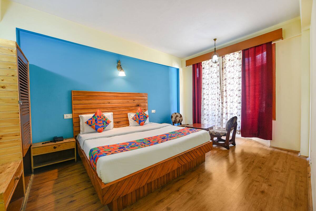 A bedroom with a wooden bed, a nightstand, a chair, and a window with red curtains.