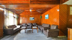 Ein gemütliches Zimmer mit Holzwänden, einem Fischgrätparkett und mehreren Sofas und Sesseln zum Sitzen.