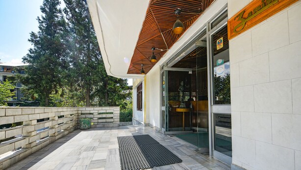 Ein Gebäudeeingang mit einer gefliesten Terrasse, einem Holz-Rolldach und einer Glasdoor.