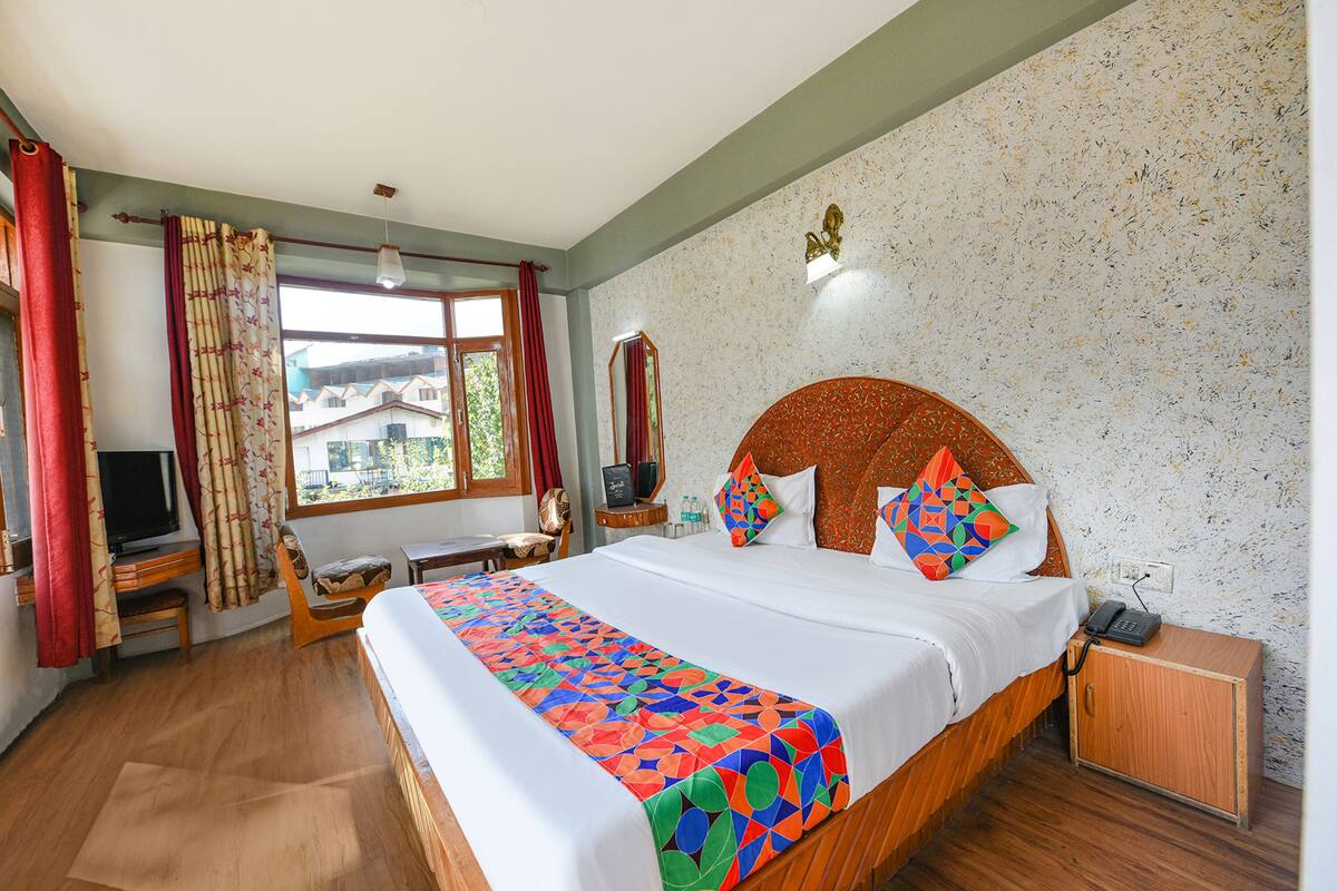 A hotel room with a large bed, a desk, a chair, a TV, and a window with curtains.