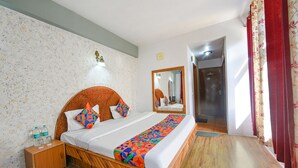 Ein Hotelzimmer mit einem hölzernen Bett, einem Spiegel, einem Nachttisch mit Wasserflaschen und einer Wand mit Muster.