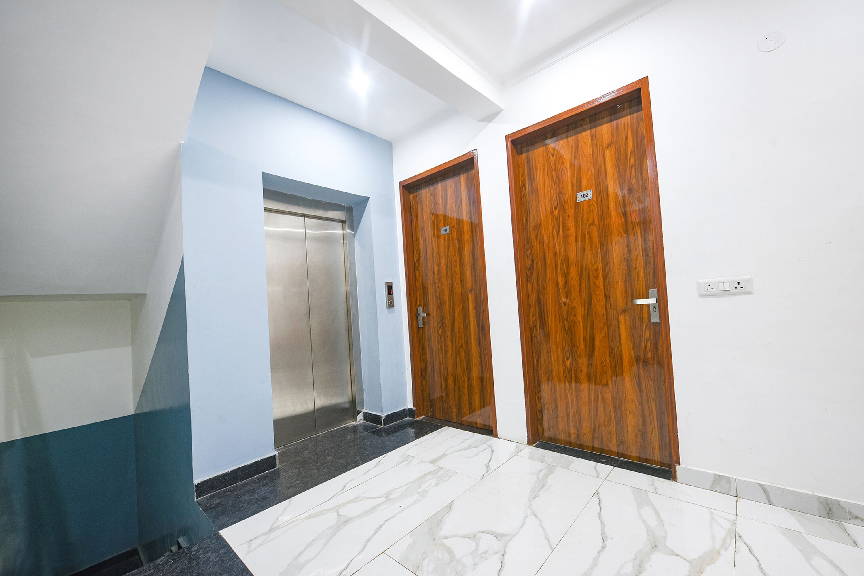 A hallway with a marble floor, two wooden doors, and an elevator.