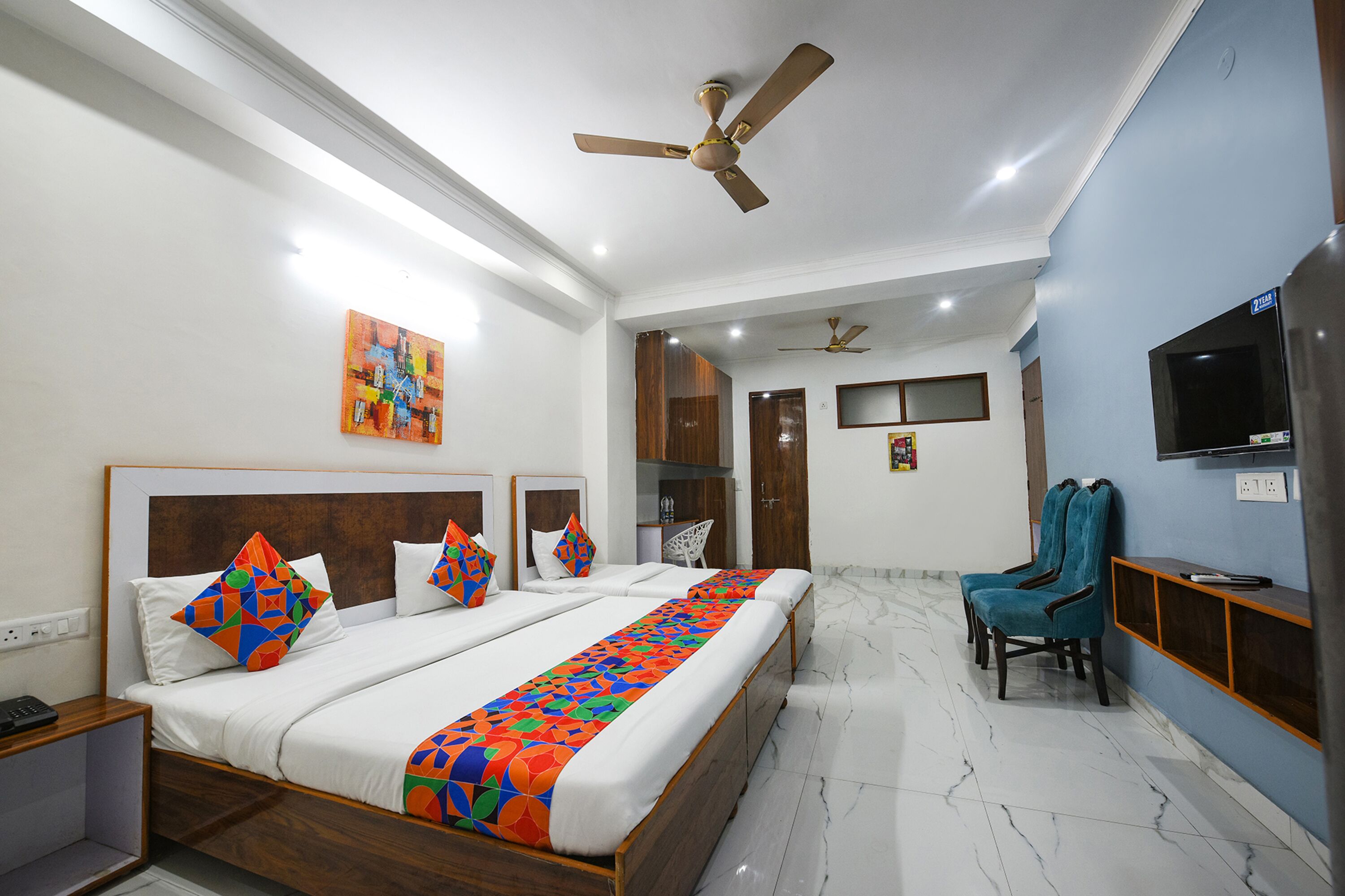 A hotel room with a large bed, a desk, a chair, a TV, and a ceiling fan.