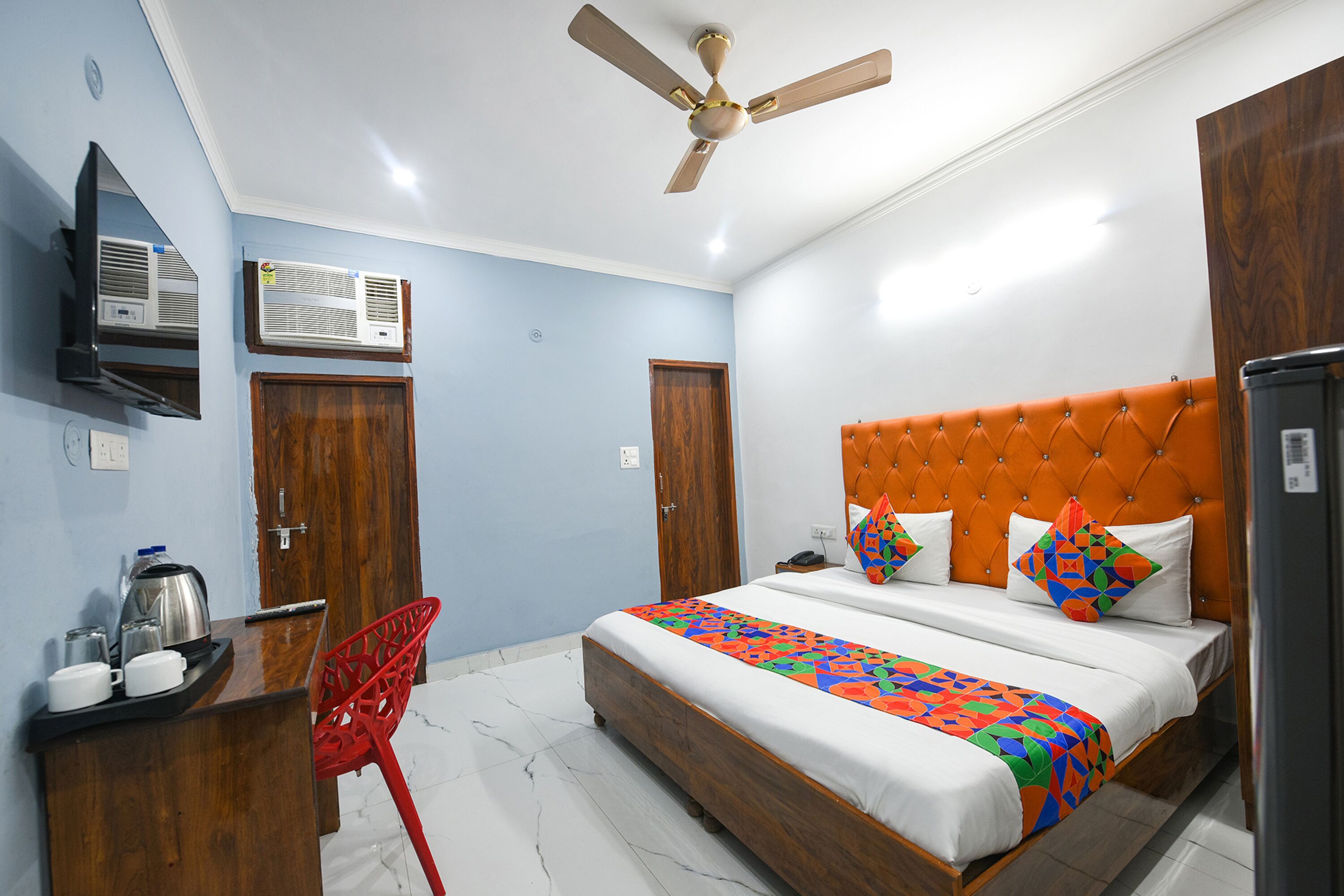 A hotel room with a bed, a desk with a chair, an air conditioning unit, and a ceiling fan.
