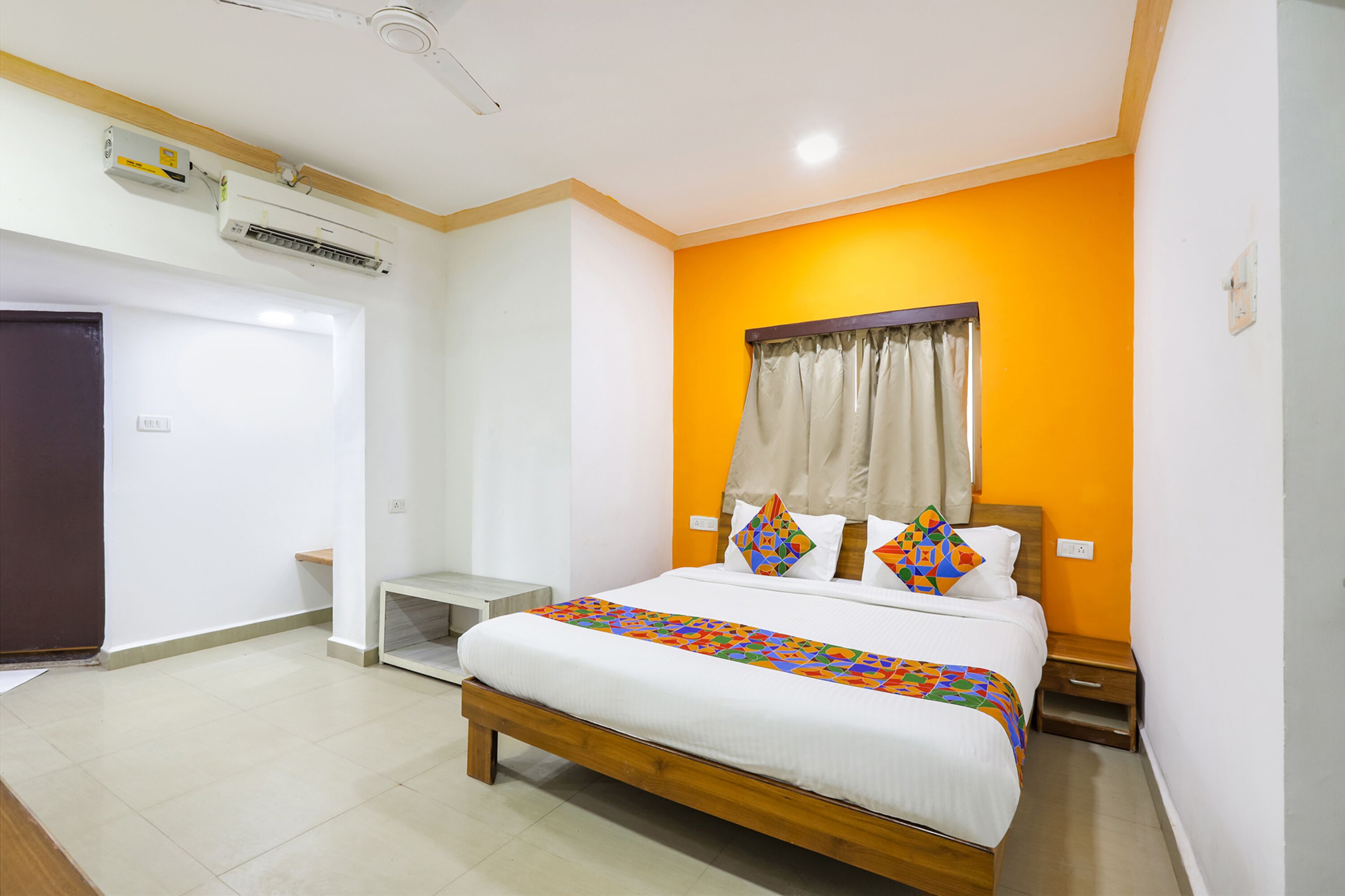 A bedroom with a bed, a nightstand, a window with curtains, and an air conditioning unit.