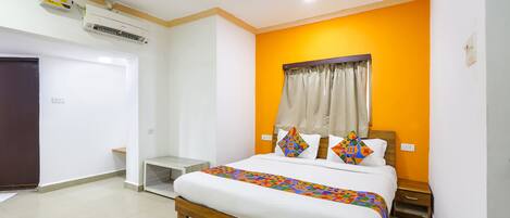 A bedroom with a bed, a nightstand, a window with curtains, and an air conditioning unit.