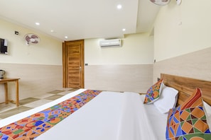 A hotel room with a bed, a wooden door, an air conditioning unit, a small table, and a wall-mounted fan. - Fabhotel Elite (Dehradun)