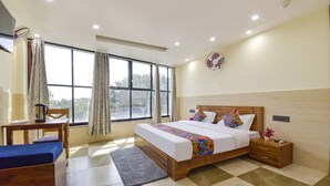 A hotel room with a bed, bedside table, and a small desk with a chair. - Fabhotel Elite (Dehradun)