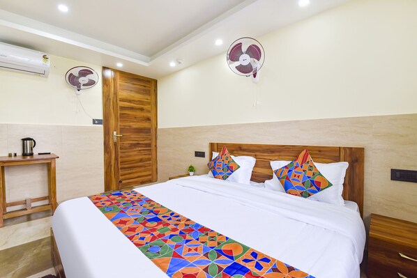 A hotel room with a bed, two wall fans, a wooden door, a small table with a kettle, and a tiled floor. - Fabhotel Elite (Dehradun)