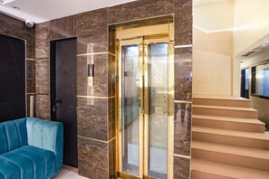 A modern interior with a blue sofa, a marble wall, and a glass elevator. - FabHotel Well Back (Mumbai)