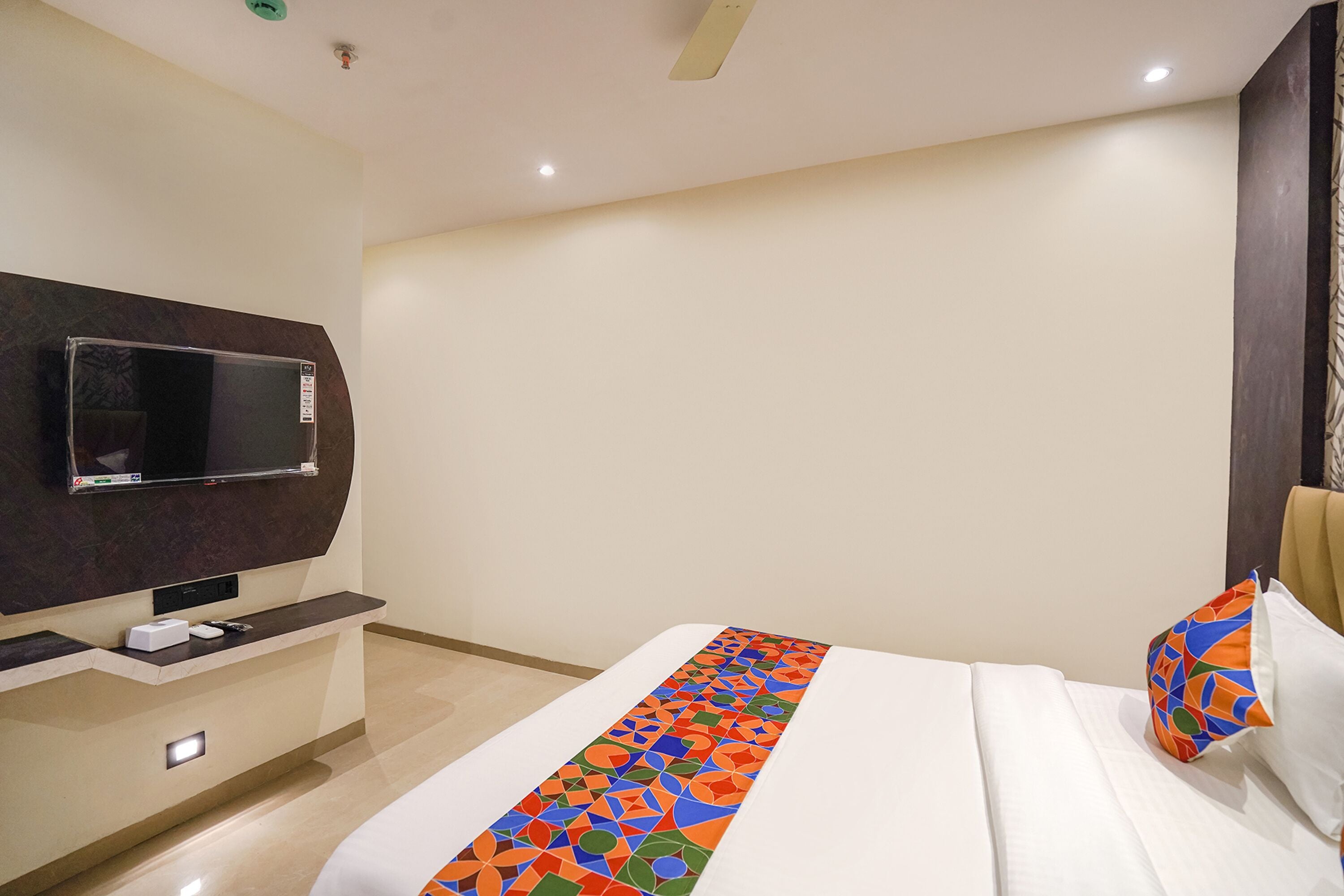 A hotel room with a bed, a TV mounted on the wall, a bedside table, and a decorative pillow.