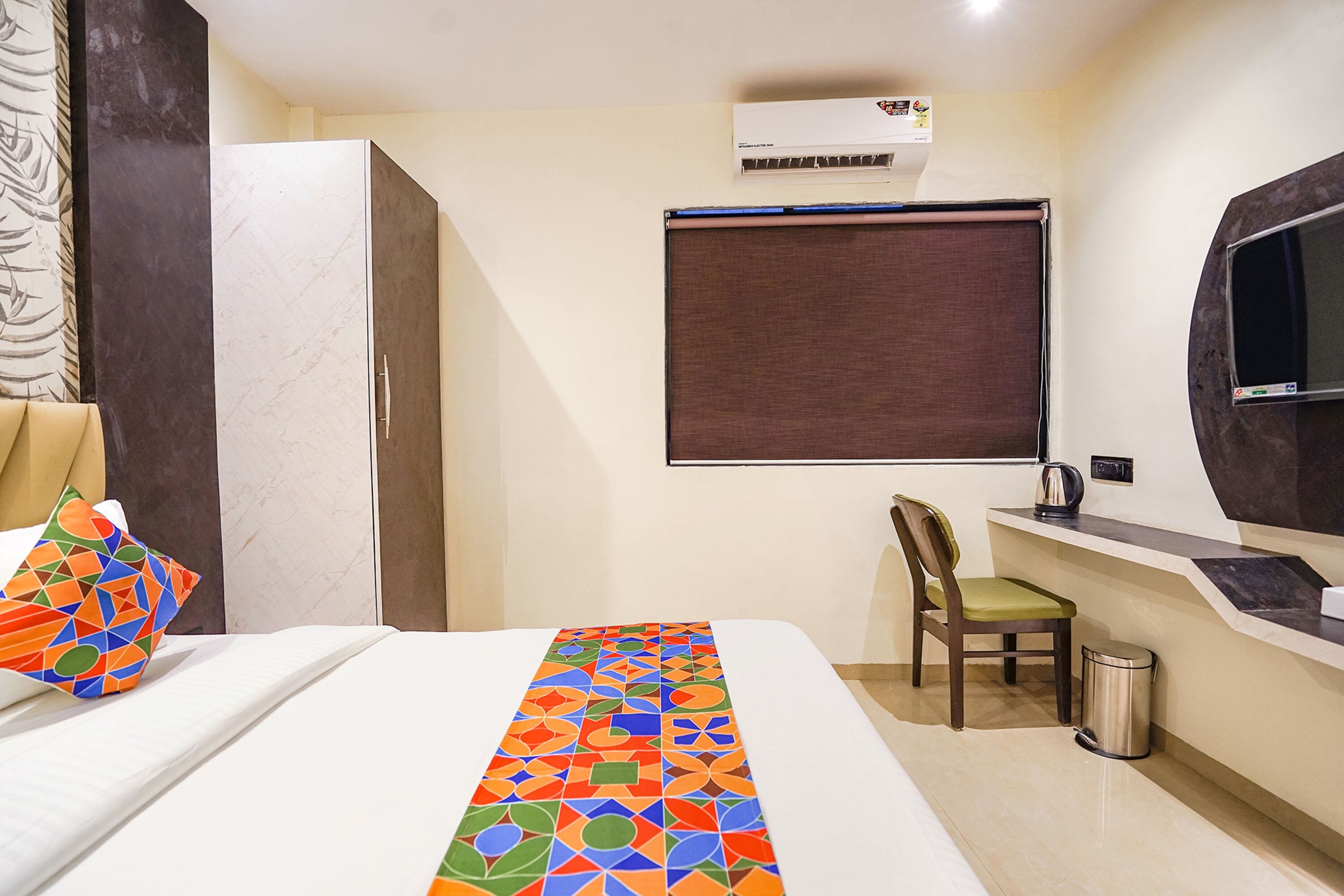 Habitación de hotel con cama, escritorio, silla, equipo de aire acondicionado y ventana con persiana.