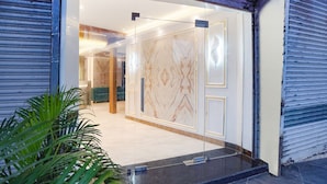 A modern hotel entrance with a glass door, a marble-patterned wall, and a green sofa inside. - Fabhotel Well Back (Mumbai)