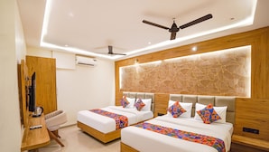 A hotel room with two beds, a wooden desk, a ceiling fan, and a stone-patterned wall. - Fabhotel Well Back (Mumbai)