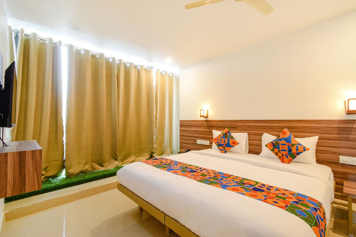 Una habitación de hotel con una cama, cortinas, un cabecero de madera y un pequeño escritorio con un televisor.