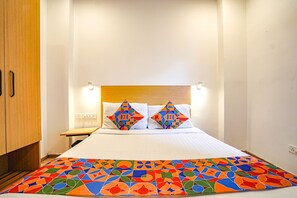 A neatly made bed with a colorful geometric-patterned bedspread, a wooden headboard, and two matching pillows. - Fabhotel Woodland (Nagpur)